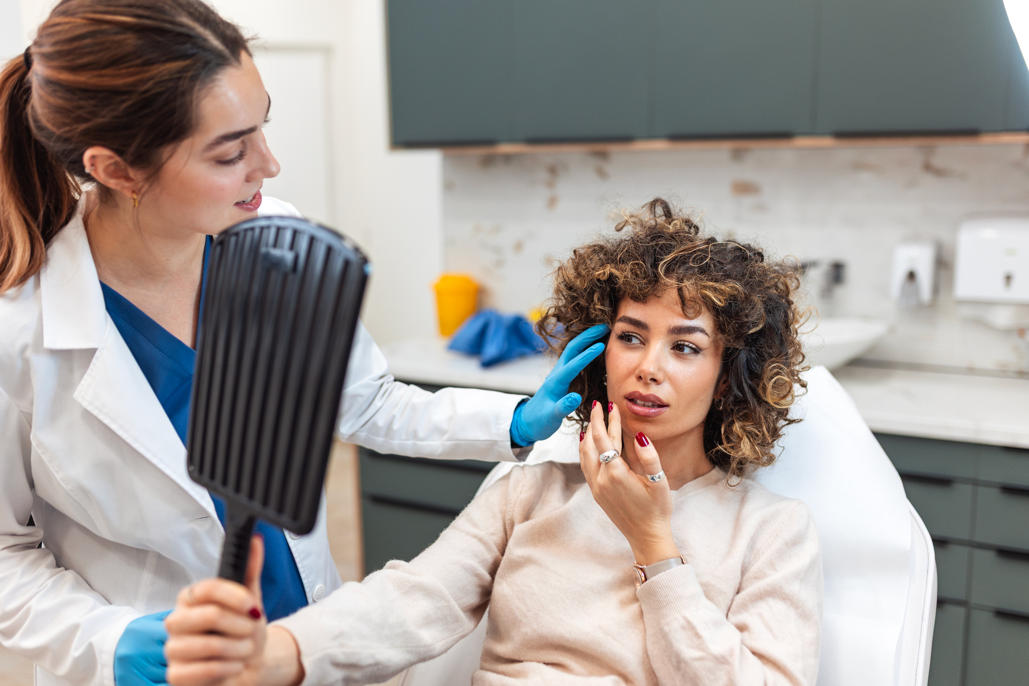 Smiling female patient looking into mirror after plastic surgery treatment